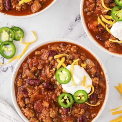 A bowl of cihli topped with sour cream and jalapenoes.