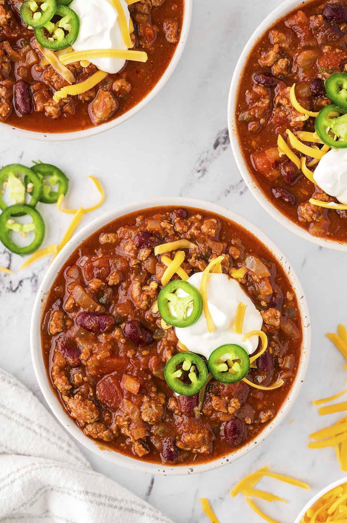 A bowl of chili topped with sour cream and sliced jalapenos.