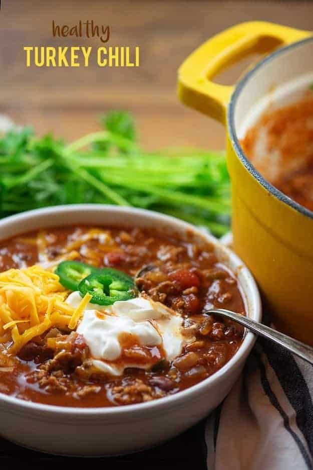 A white bowl of chili next to a yellow pot.