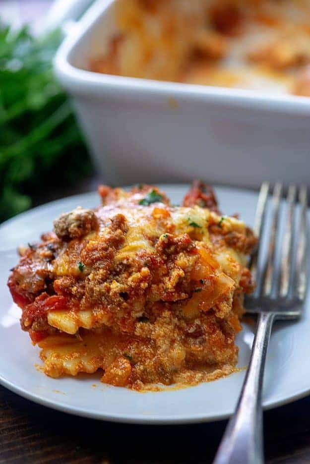 A square piece of lasagna on a whtie plate.