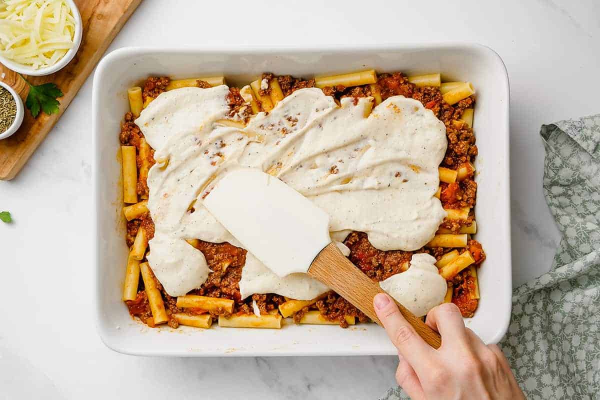 woman spreading bechamel sauce over pasta.