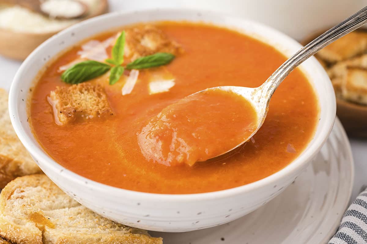 Homemade tomato soup on a spoon over a bowl.