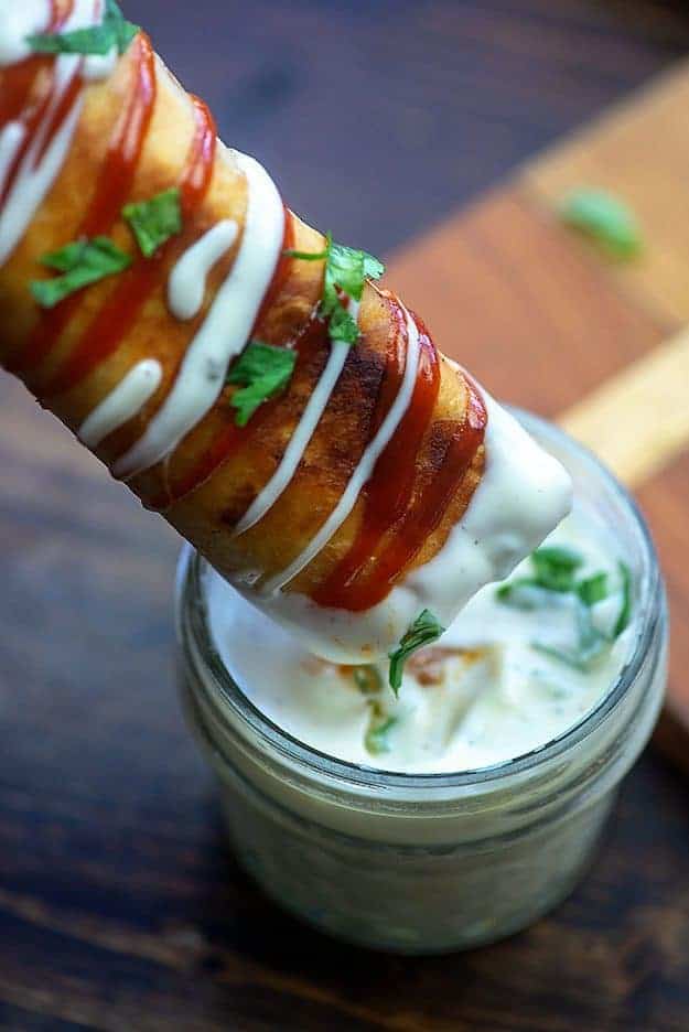 A taquito being dipped into a jar of ranch dressing.