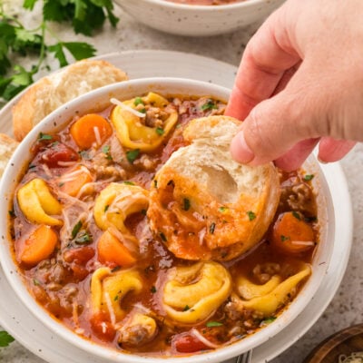 Hand dipping bread into bowl of sausage tortellini soup.
