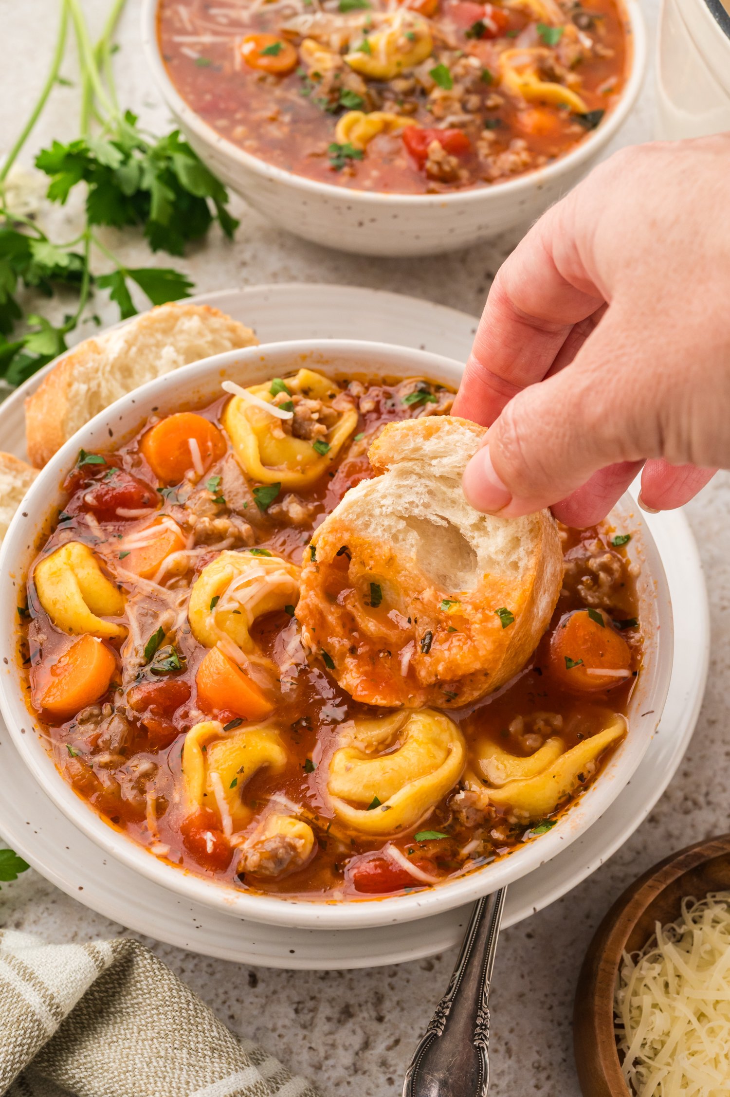 Hand dipping bread into bowl of sausage tortellini soup.