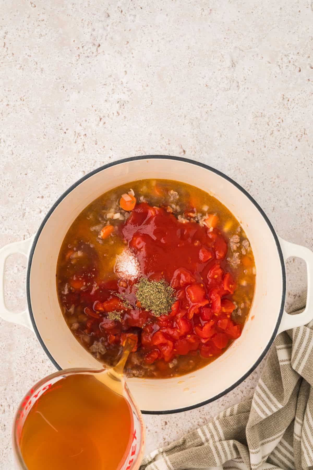 Beef broth being poured into pot of sausage and tortellini soup.
