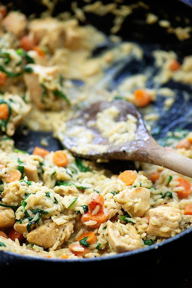 Wooden spoon stirring chicken in and rice in a cast-iron skillet.