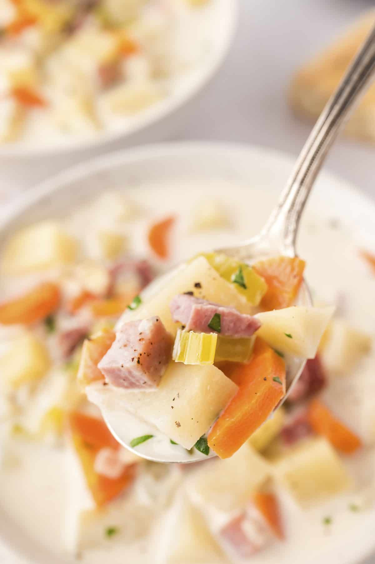 Ham and potato soup on spoon.