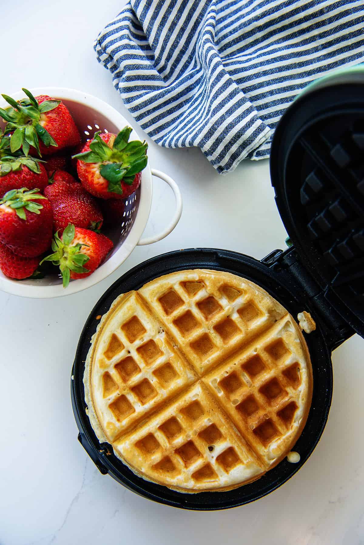 waffle in waffle iron next to strawberries.