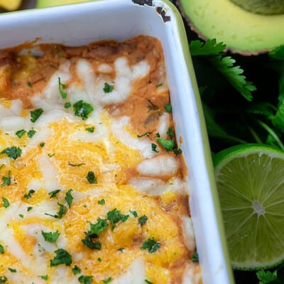 A close up of beans and cheese in a baking pan next to sliced limes.