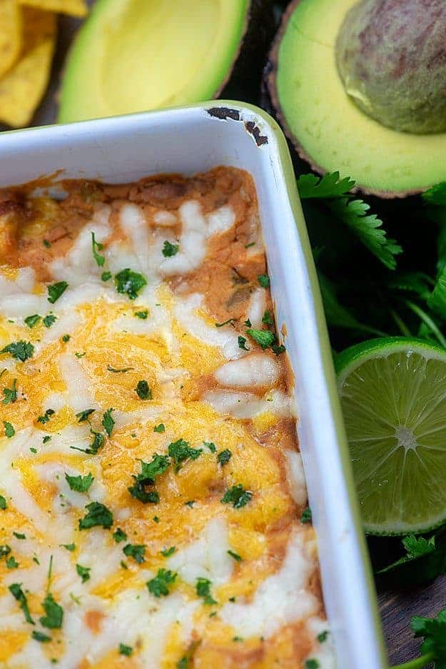 A close up of beans and cheese in a baking pan next to sliced limes.