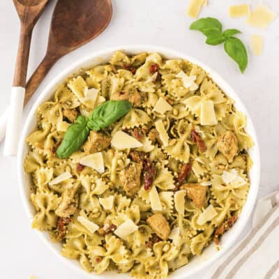 Chicken pesto pasta in white serving bowl with wooden spoons.