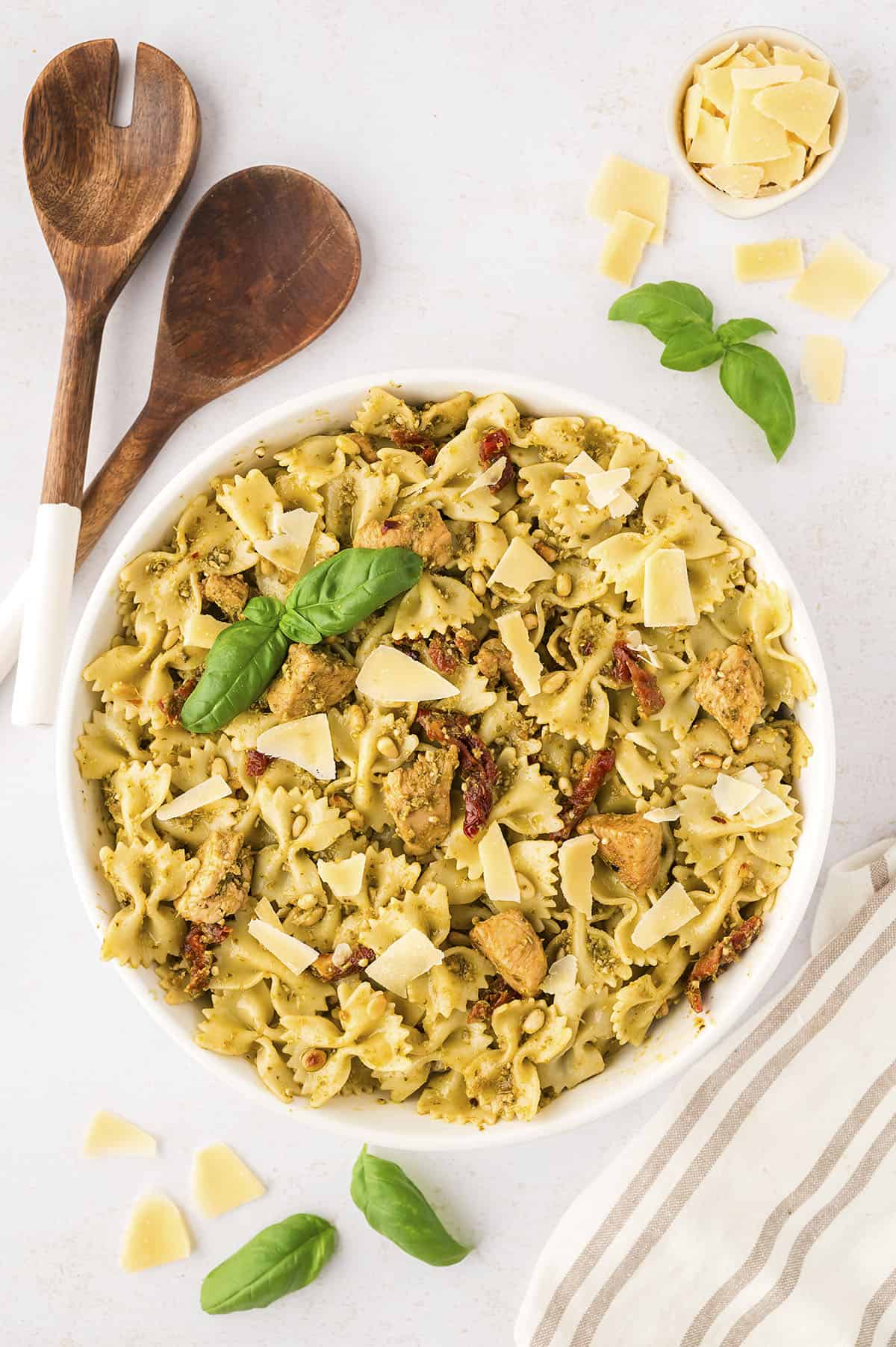 Chicken pesto pasta in white serving bowl with wooden spoons.