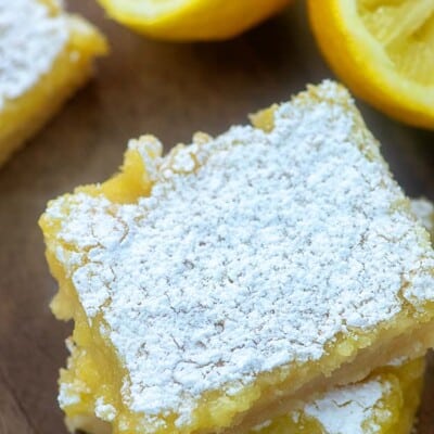 Two square lemon bars stacked on a cutting board.