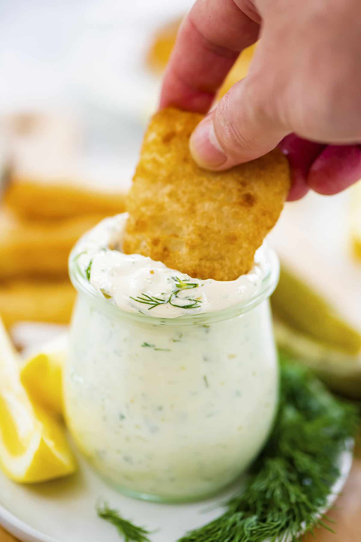 Hand dipping fish in tartar sauce.