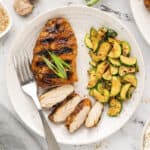 Sliced teriyaki chicken on plate with cucumbers.