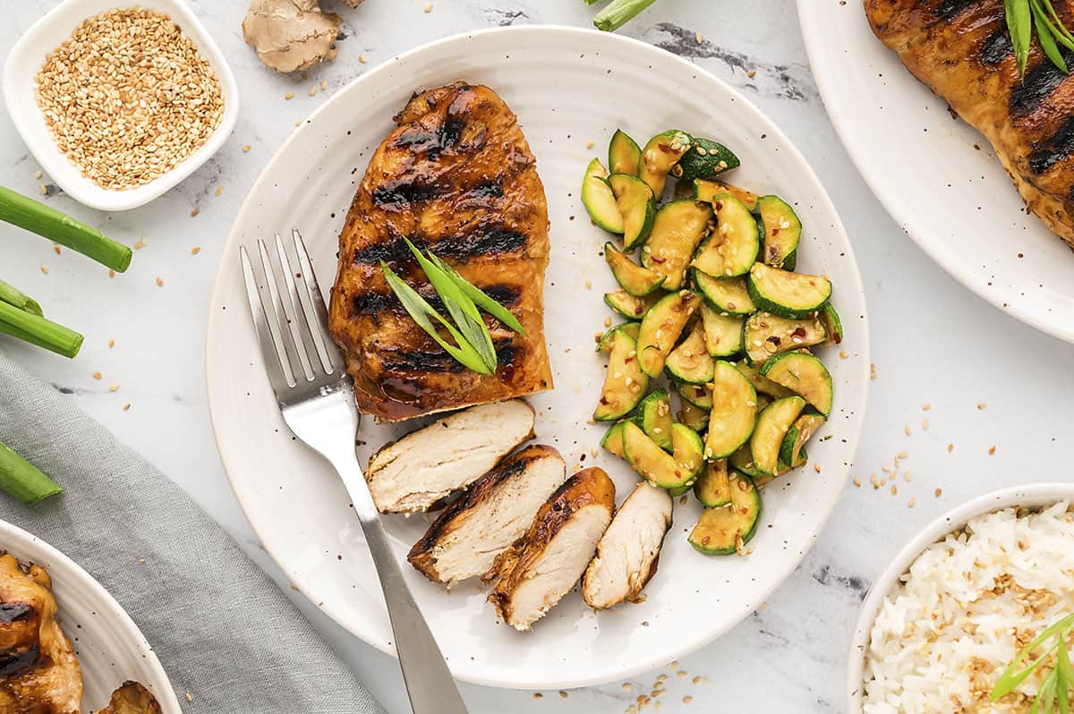 Sliced teriyaki chicken on plate with cucumbers.