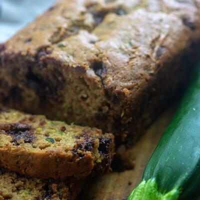 A loaf of zucchini bread on a cutting board with a few slices made in the loaf.