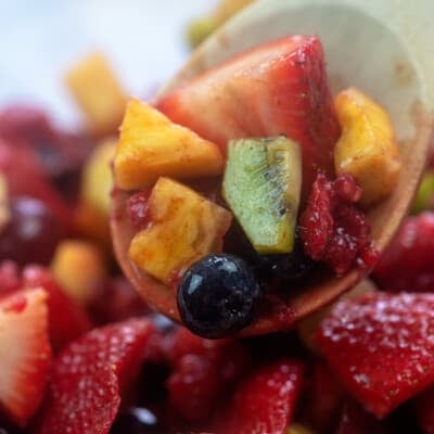 Wooden spoon with fruit salad on top of a bowl of fruit salad.