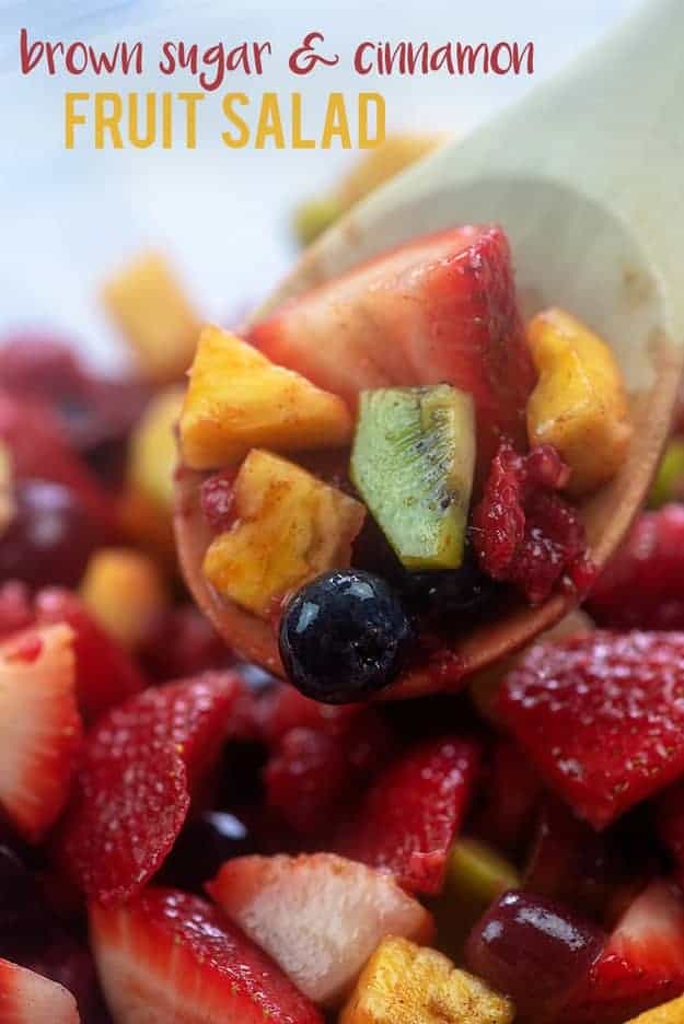 Wooden spoon with fruit salad on top of a bowl of fruit salad.