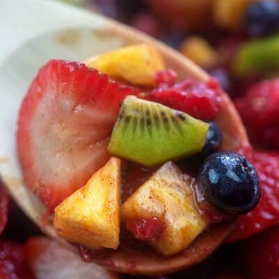 A wooden spoon holding up fruit salad to the camera.