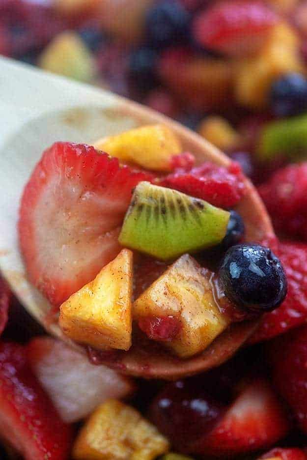 A wooden spoon holding up fruit salad to the camera.