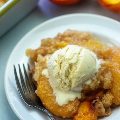 Peach cobbler topped with ice cream on a white plate