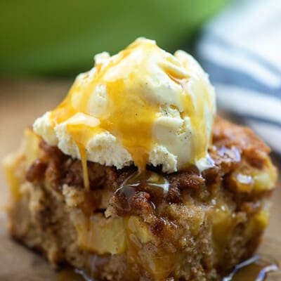 A close up of a piece of cake on a plate, with ice cream and caramel on top.