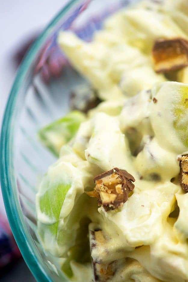 Close up of a bowl of apple salad with chunks of snickers in it.