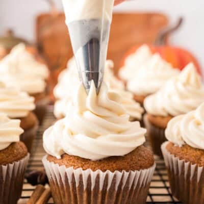 Pumpkin cupcakes with cream cheese frosting being piped over the top.