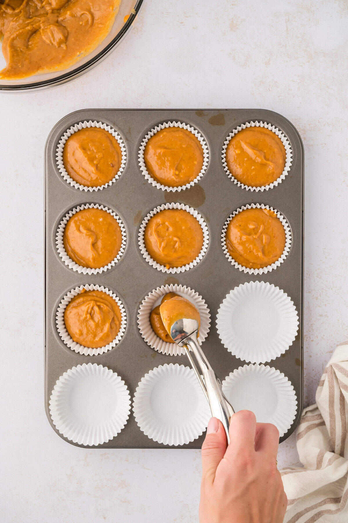 Muffin tin lined with papers being filled with pumpkin cupcake batter.