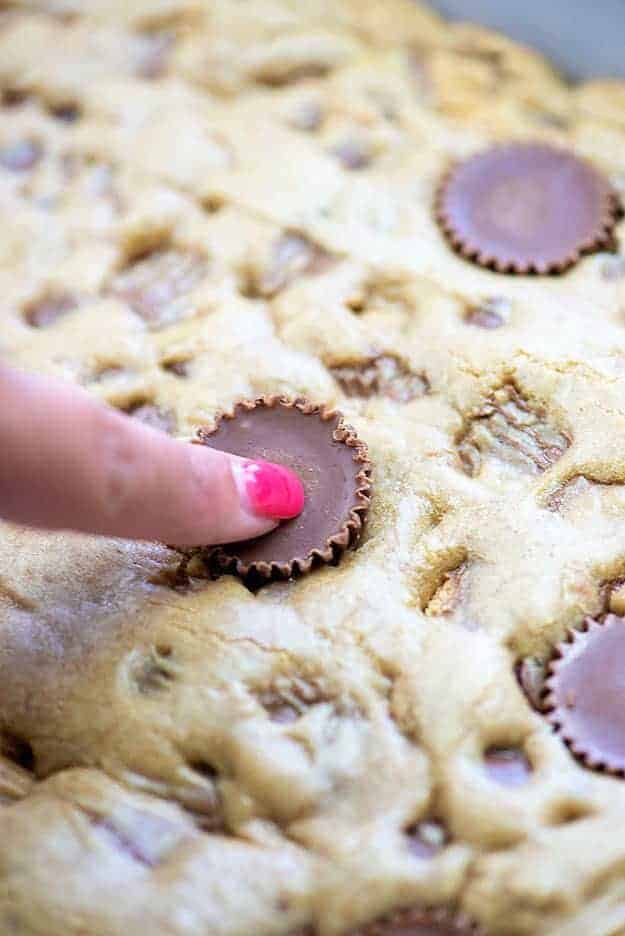 A woman\'s finger pressing a peanut butter cup into a blondie.