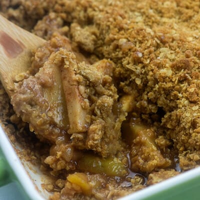A wooden spoon scooping apple crisp from a baking dish.