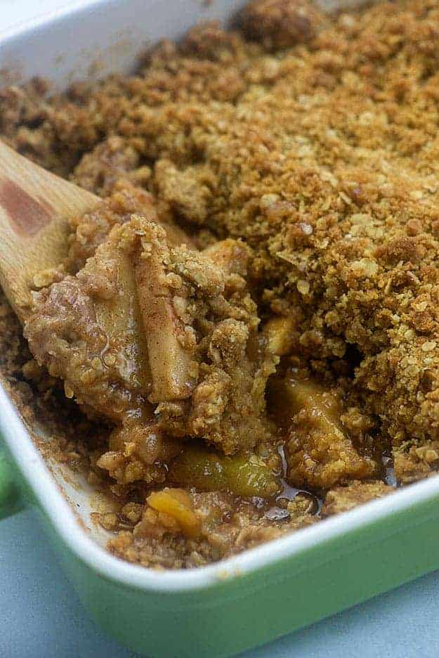 A wooden spoon scooping apple crisp from a baking dish.