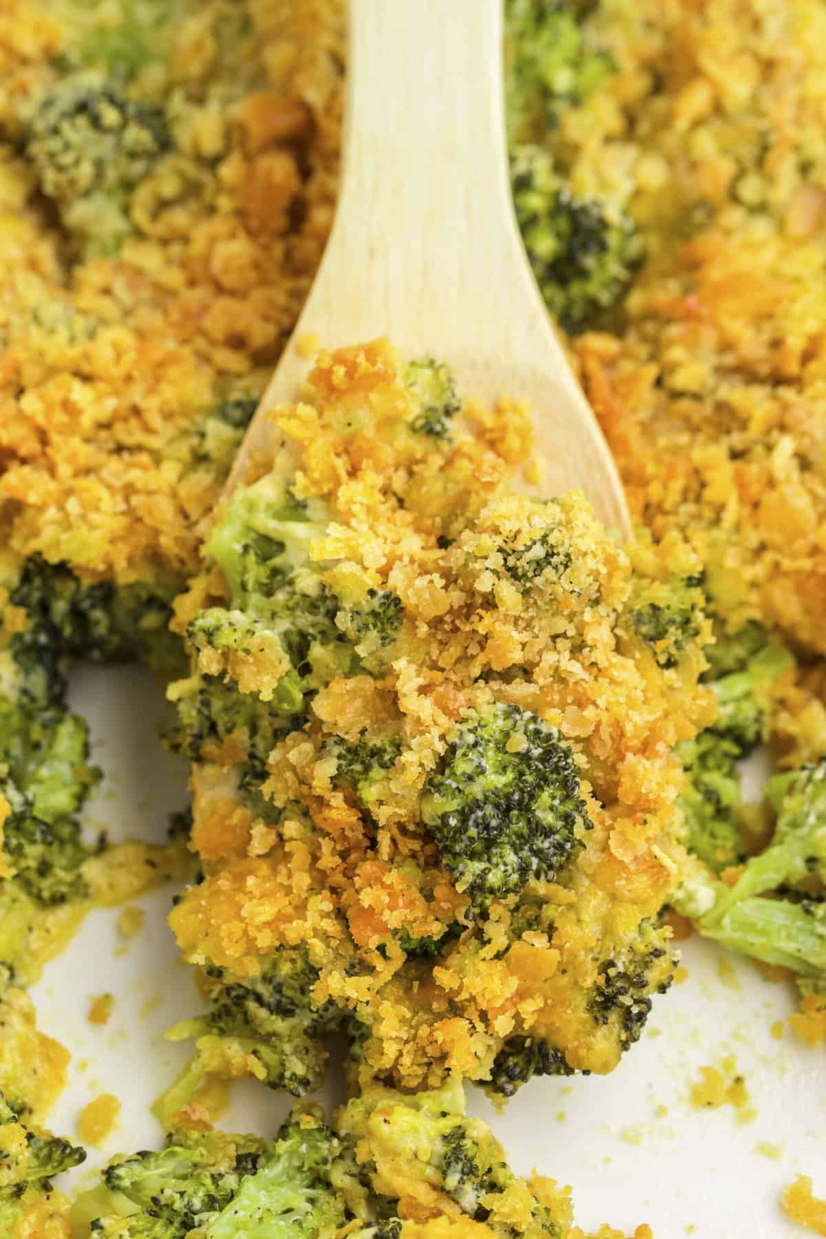 Broccoli cheese casserole on wooden spoon in baking dish.