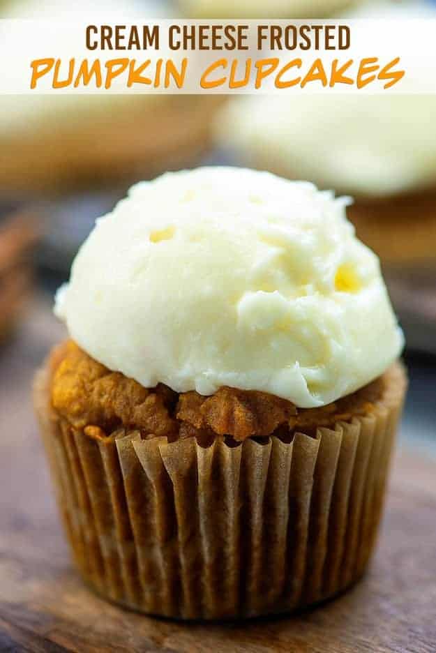 A close up of a wrapped pumpkin cupcake with white frosting on top.