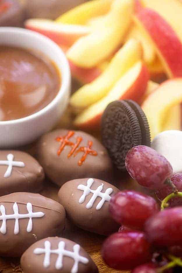 Close up of cookies, grapes, caramel dip, and football-shaped candy.