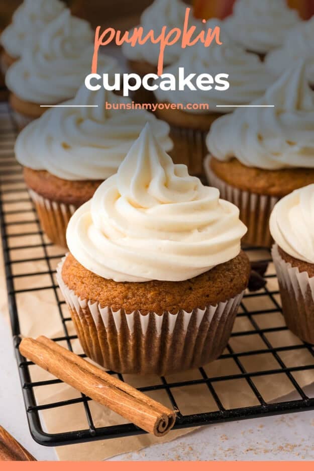 Pumpkin cupcake topped with cream cheese frosting on wire rack.