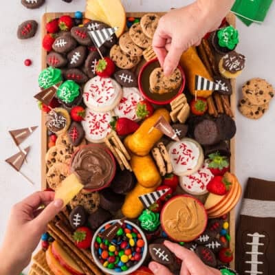 Hands grabbing snacks off football snack board.