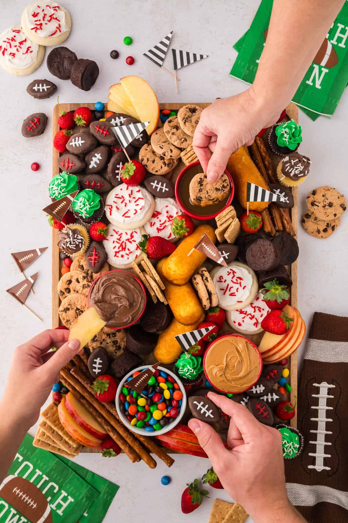Hands grabbing snacks off football snack board.