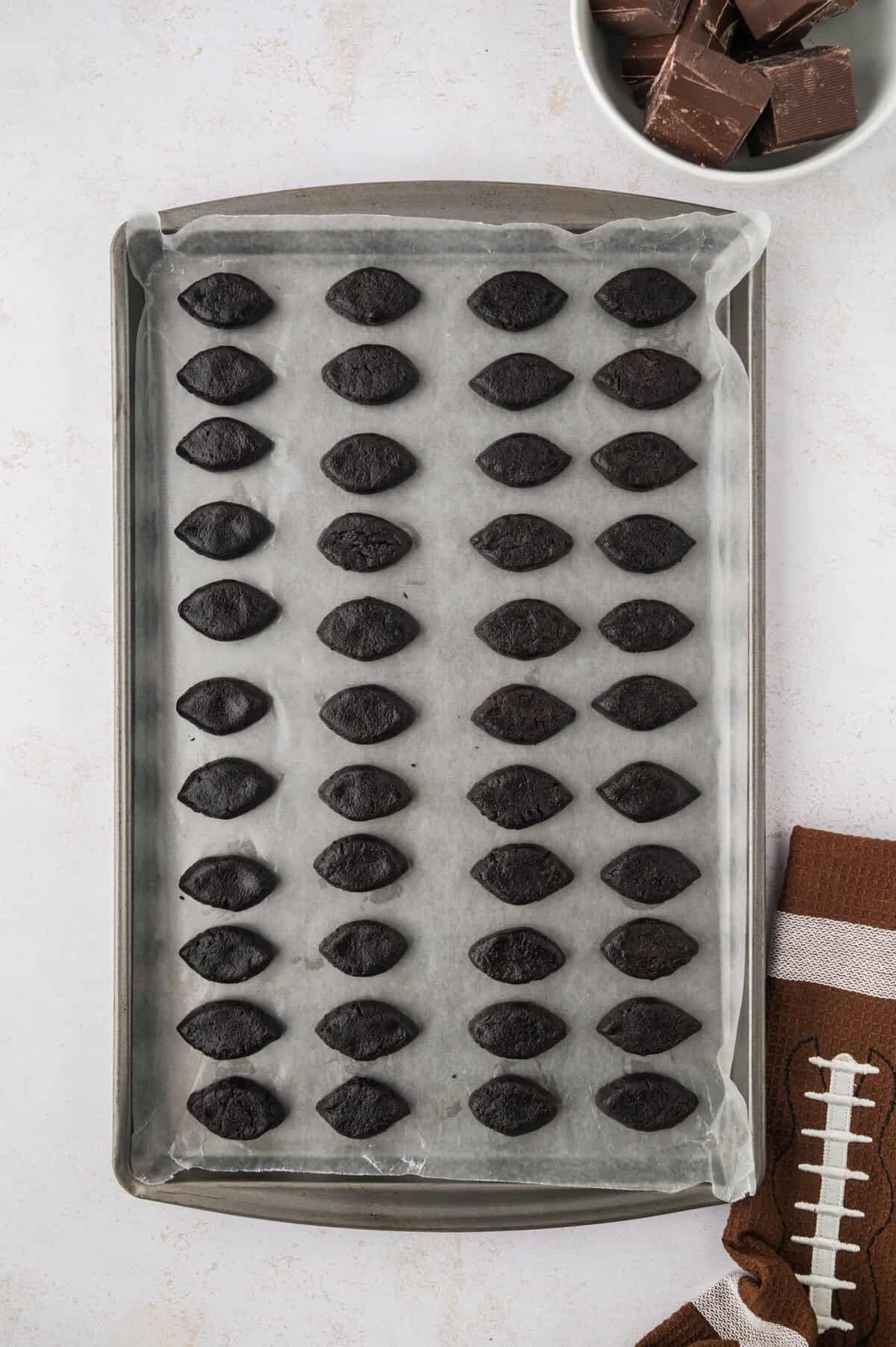 Oreo balls shaped like football on baking sheet.