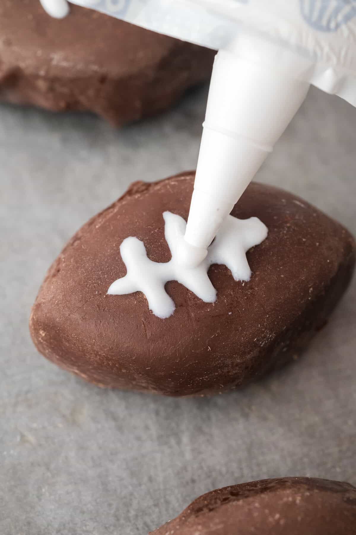 Stitches being piped on football shaped oreo ball.