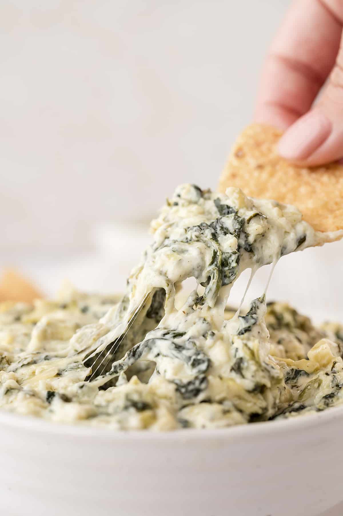 Hand dipping a chip into spinach artichoke dip.