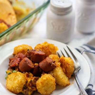 Chili, tater tots, and hot dog pieces on a small white plate.