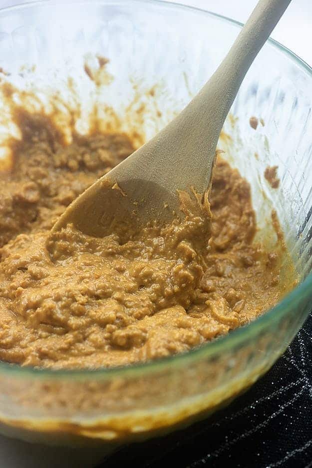 Clear glass bowl of peanut butter dough and a wooden spoon in it.