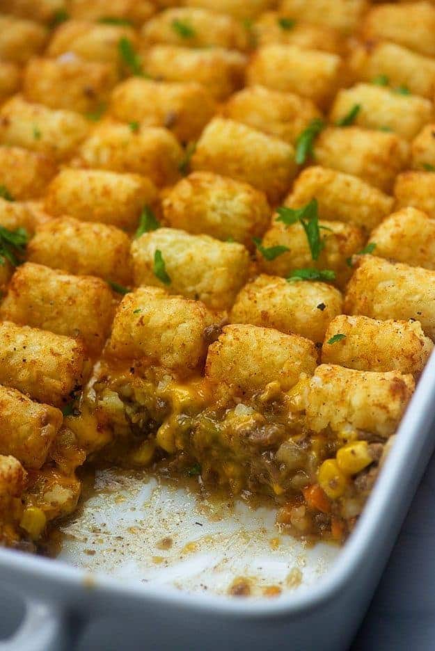 A white baking sheet of tater tots with a serving missing.