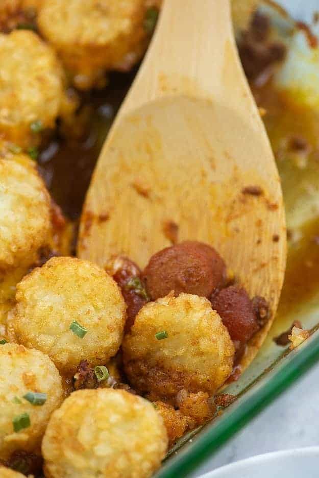 Tater tots and hot dogs on a wooden spoon.