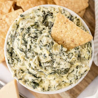Overhead view of the best spinach artichoke dip recipe in a white bowl surrounded by tortilla chips.