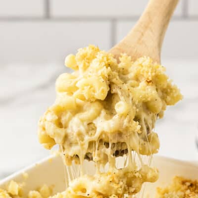 Creamy baked mac and cheese on wooden spoon over casserole dish.