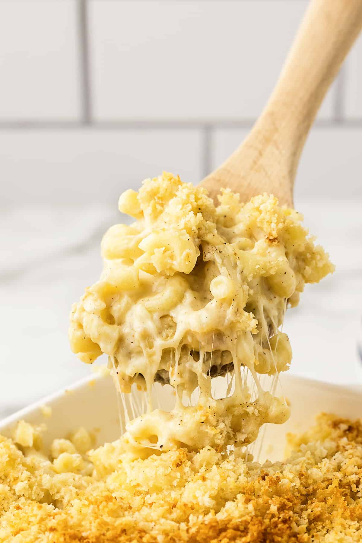 Creamy baked mac and cheese on wooden spoon over casserole dish.